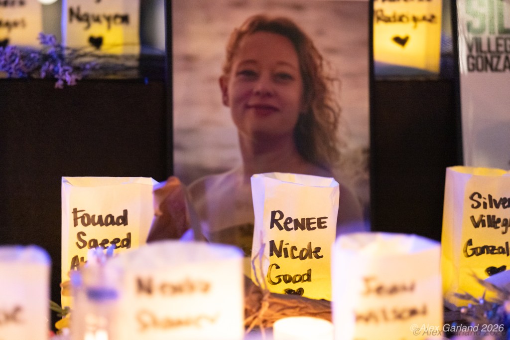 A photo of a woman with curly hair displayed among memorial candles, with names written on the candle bags, including Renee Nicole Good, Fouad Saeed Abdo, and others.